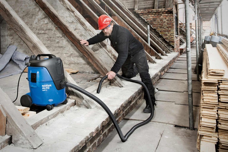 Un ouvrier utilise un aspirateur eau et poussière de Nilfisk Alto pour nettoyer un chantier.