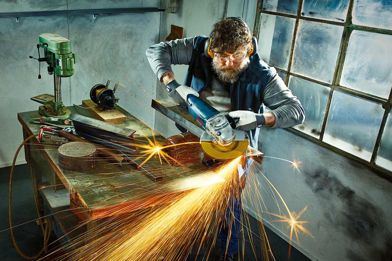 Un homme travaille avec une meuleuse d'angle dans un atelier et des étincelles se produisent.