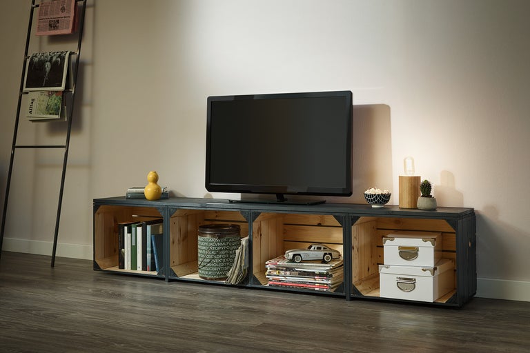 Salon avec télévision sur un meuble bas en caisses en bois et présentoir à journaux.