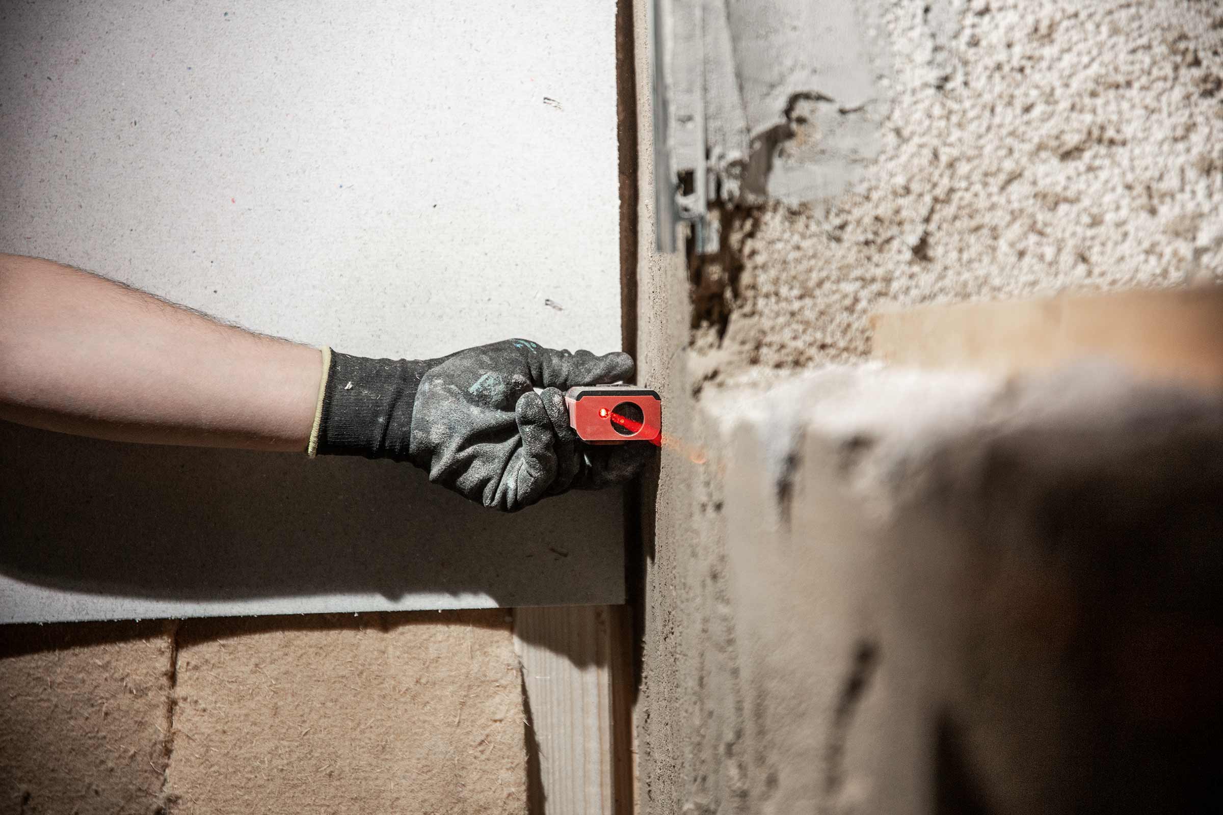 Une main gantée utilise un niveau laser sur un mur.