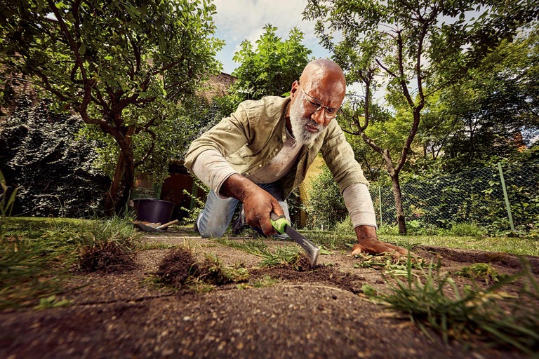 Un homme agenouillé dans le jardin utilise un outil de jardin à main pour l'entretien de la pelouse.