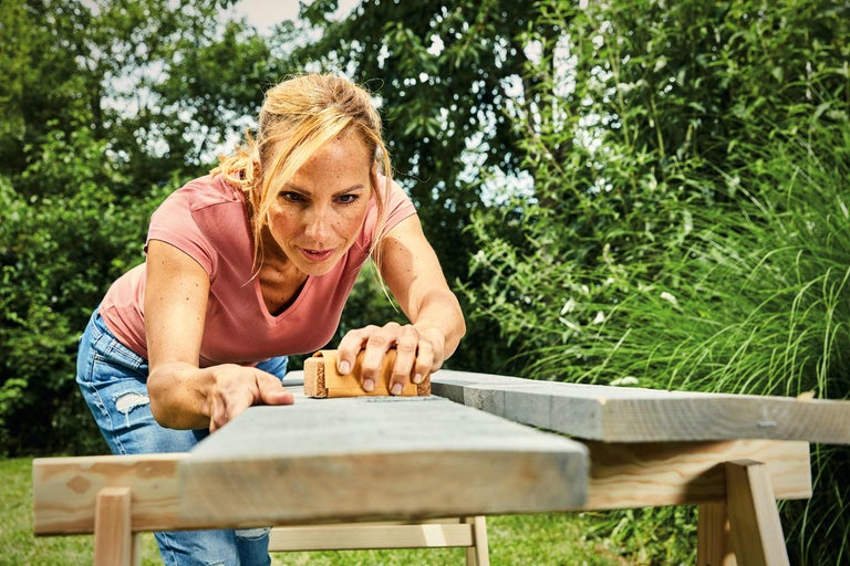 Femme ponçant une planche de bois à l'extérieur avec une cale à poncer sur un établi