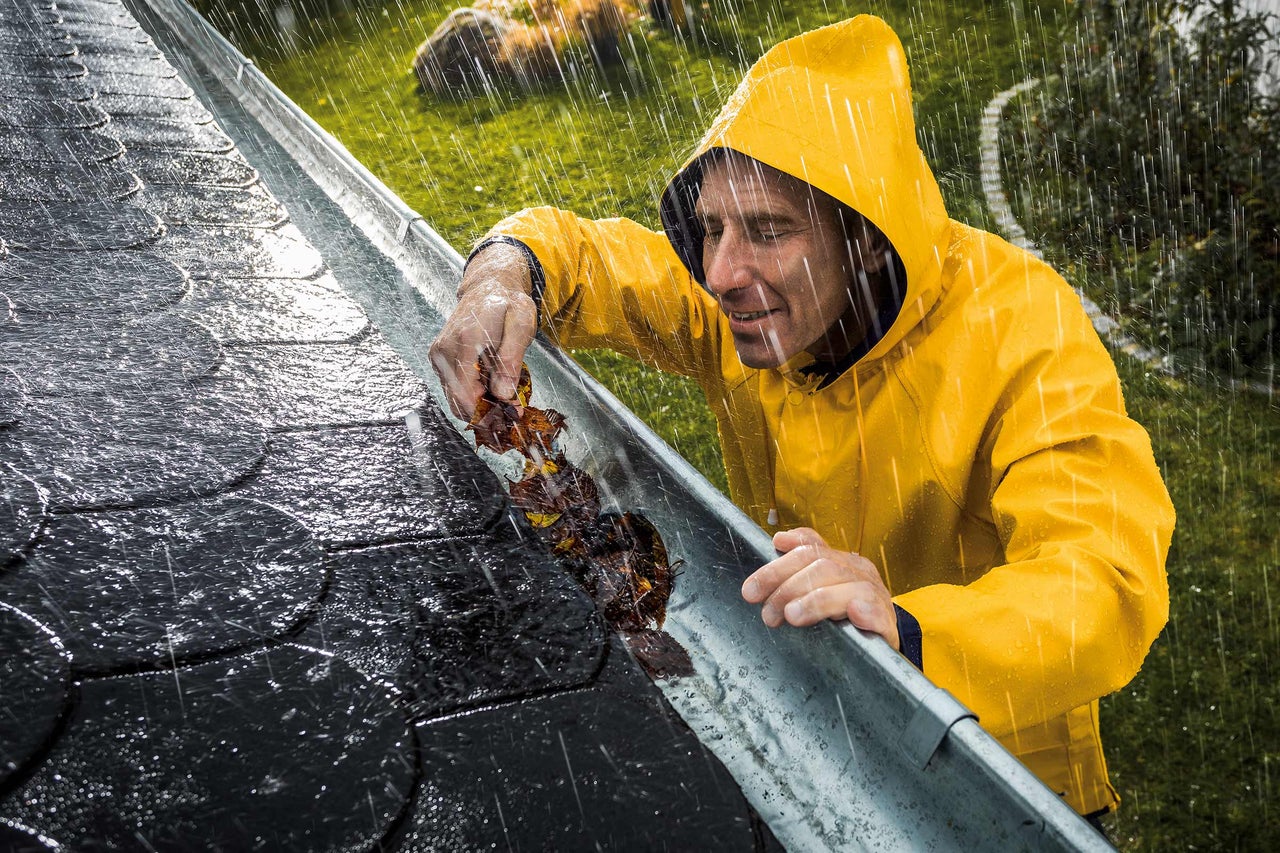 Homme en vêtements de pluie nettoyant les feuilles d'une gouttière