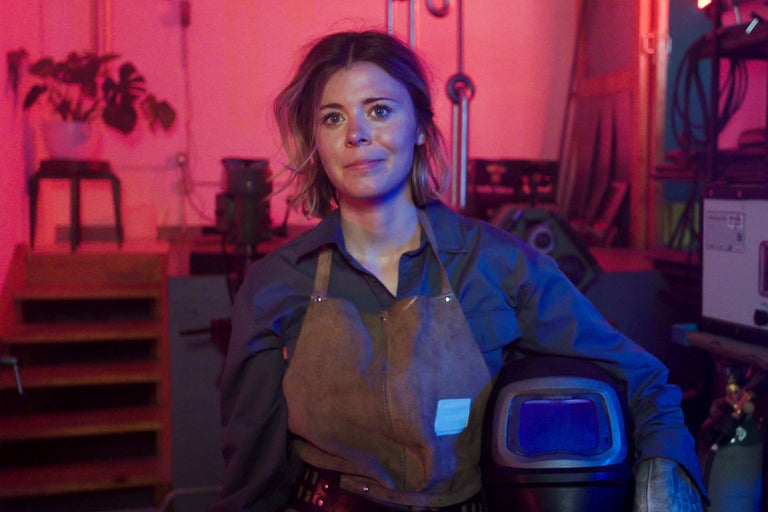 Femme avec casque de soudeur, tablier en cuir et gants dans l'atelier