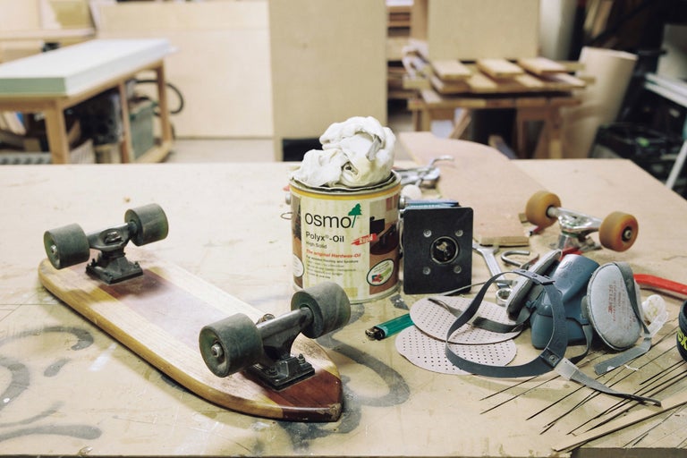 Scène d'atelier avec skateboard, boîte d'huile-cire dure Osmo, masque respiratoire et outils sur un établi