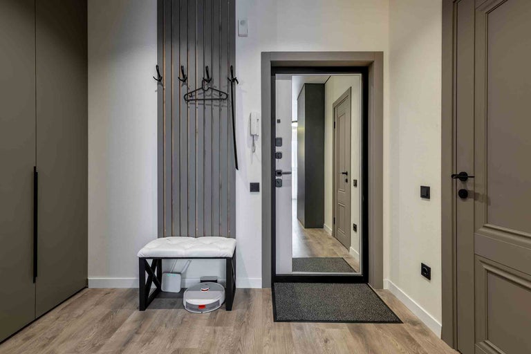 Espace d'entrée avec porte-manteau, banc, miroir et robot aspirateur.