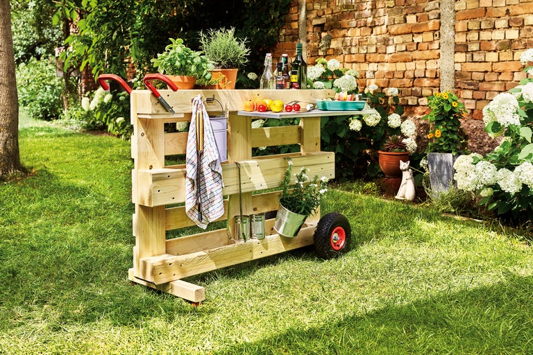 Un bar de jardin mobile en bois avec des roues et un plan de travail se trouve dans le jardin.
