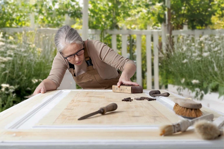 Femme ponçant une porte en bois avec du papier de verre et des outils