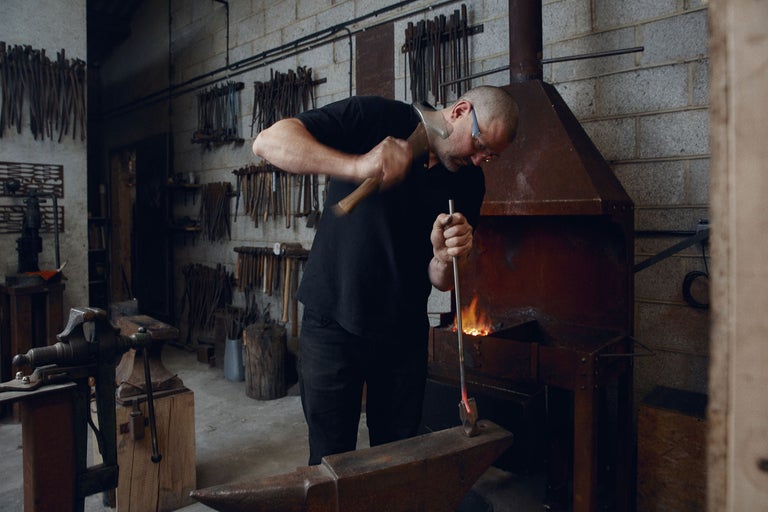 Ein Schmied bearbeitet glühendes Metall mit einem Hammer an einem Amboss in seiner Werkstatt.