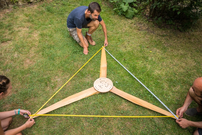 Drei Personen messen ein Windrad auf einer Rasenfläche.
