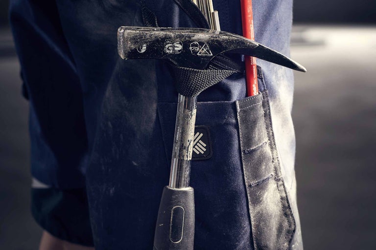 Gros plan sur un pantalon de travail avec porte-marteau contenant un marteau et un stylo.