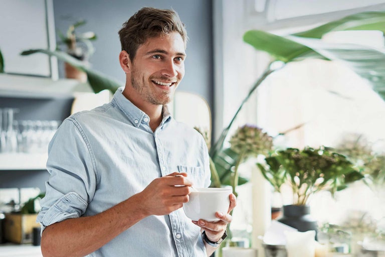 Lächelnder Mann mit Müslischale in heller Küche mit Pflanzen
