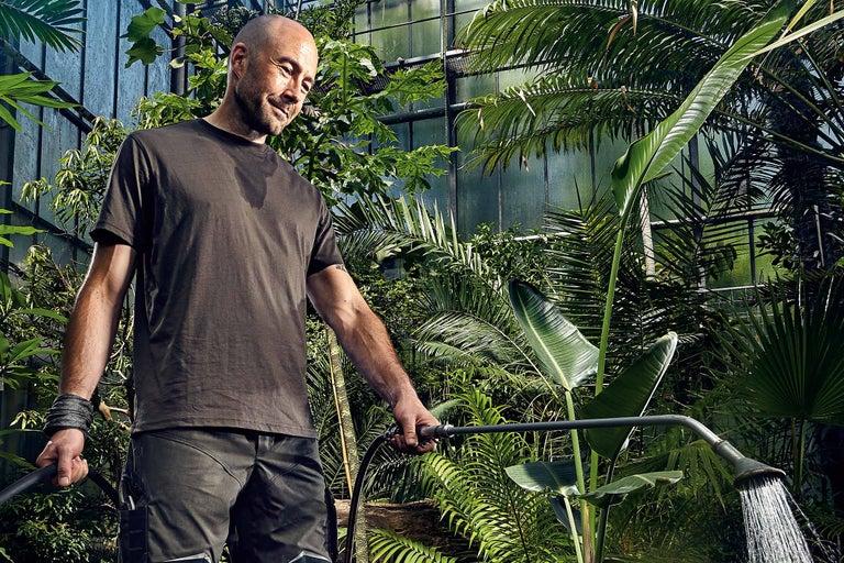 Un homme arrose des plantes avec un dispositif d'arrosage dans un jardin.