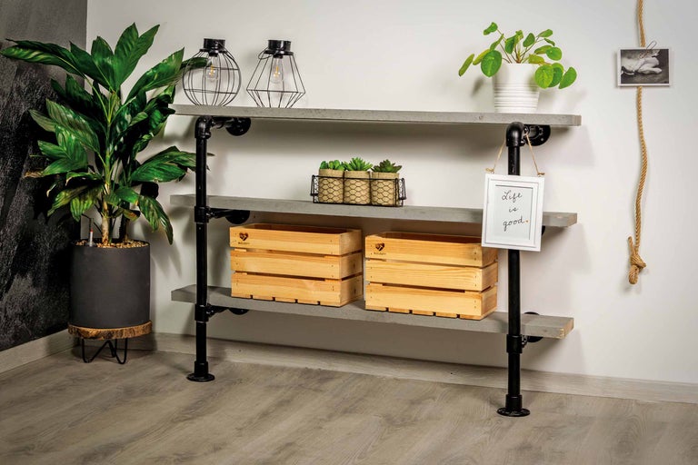 Étagère à trois niveaux en bois et tubes métalliques noirs, décorée de plantes, de caisses en bois, de lampes et d'un cadre