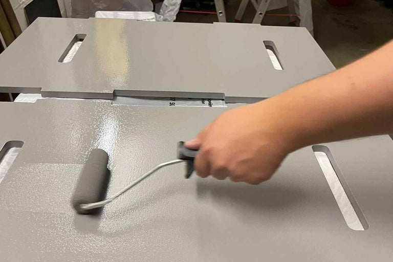 Person streicht Holzplatten mit Farbroller