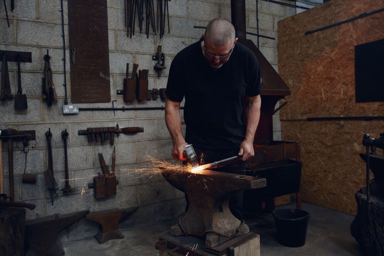 Ein Schmied bearbeitet glühendes Metall auf einem Amboss in einer Werkstatt.