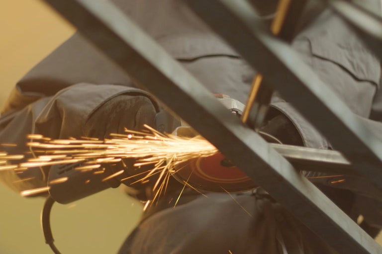 Un homme meule du métal avec une meuleuse d'angle, ce qui produit des étincelles.