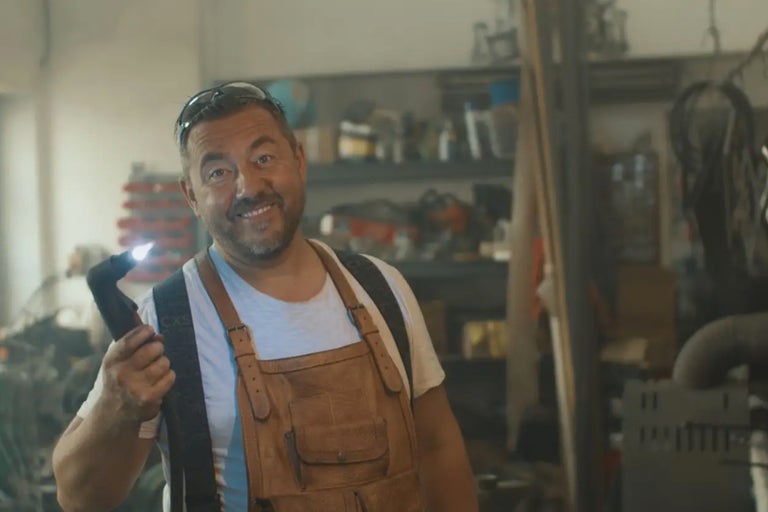 Un homme avec une lampe frontale et une salopette en cuir dans un atelier.