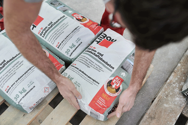 Une personne manipule des sacs de béton d'aménagement paysager et de jardin sur une palette