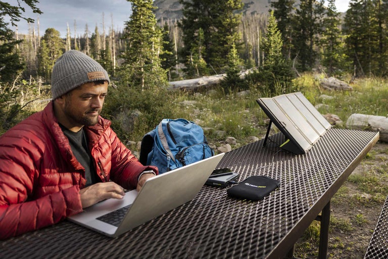 Un homme travaille sur un ordinateur portable avec un panneau solaire portable sur une table à l'extérieur