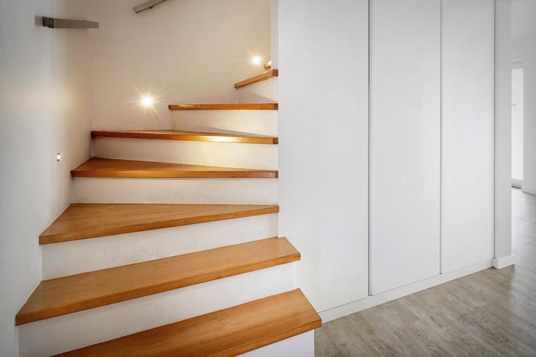 Escalier en colimaçon avec marches en bois et éclairage intégré à côté d'une armoire blanche.