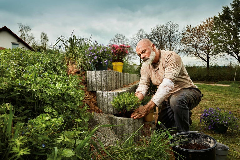 Un homme plante un mur de jardin en blocs de béton avec des plantes.