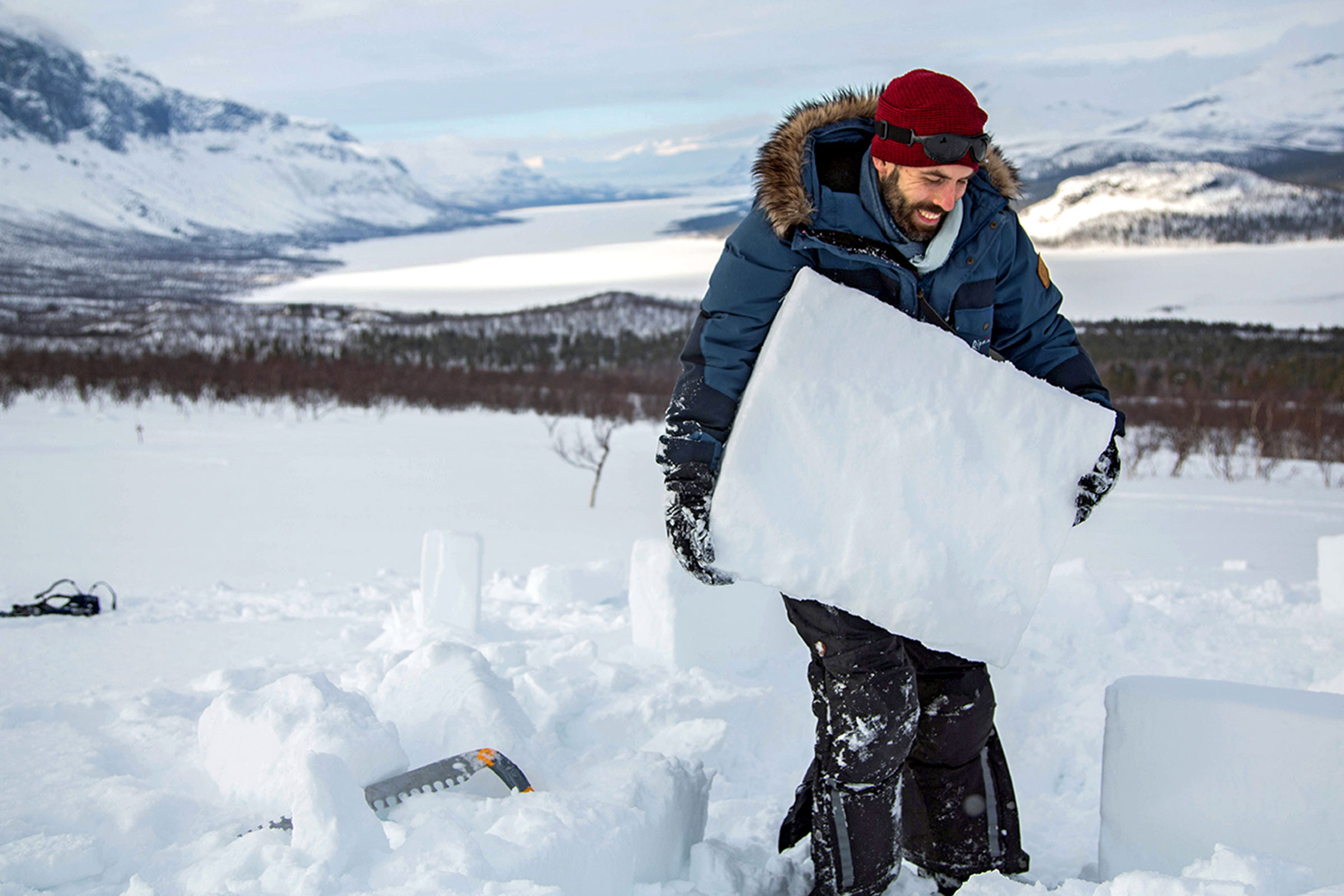 Mann trägt einen Eisblock in einer verschneiten Winterlandschaft.
