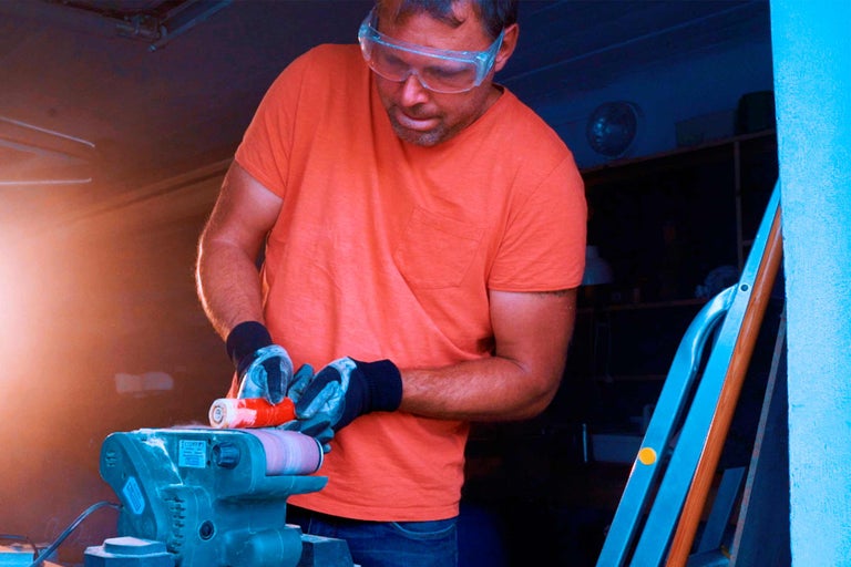 Homme ponçant une pièce avec une ponceuse à bande dans un atelier