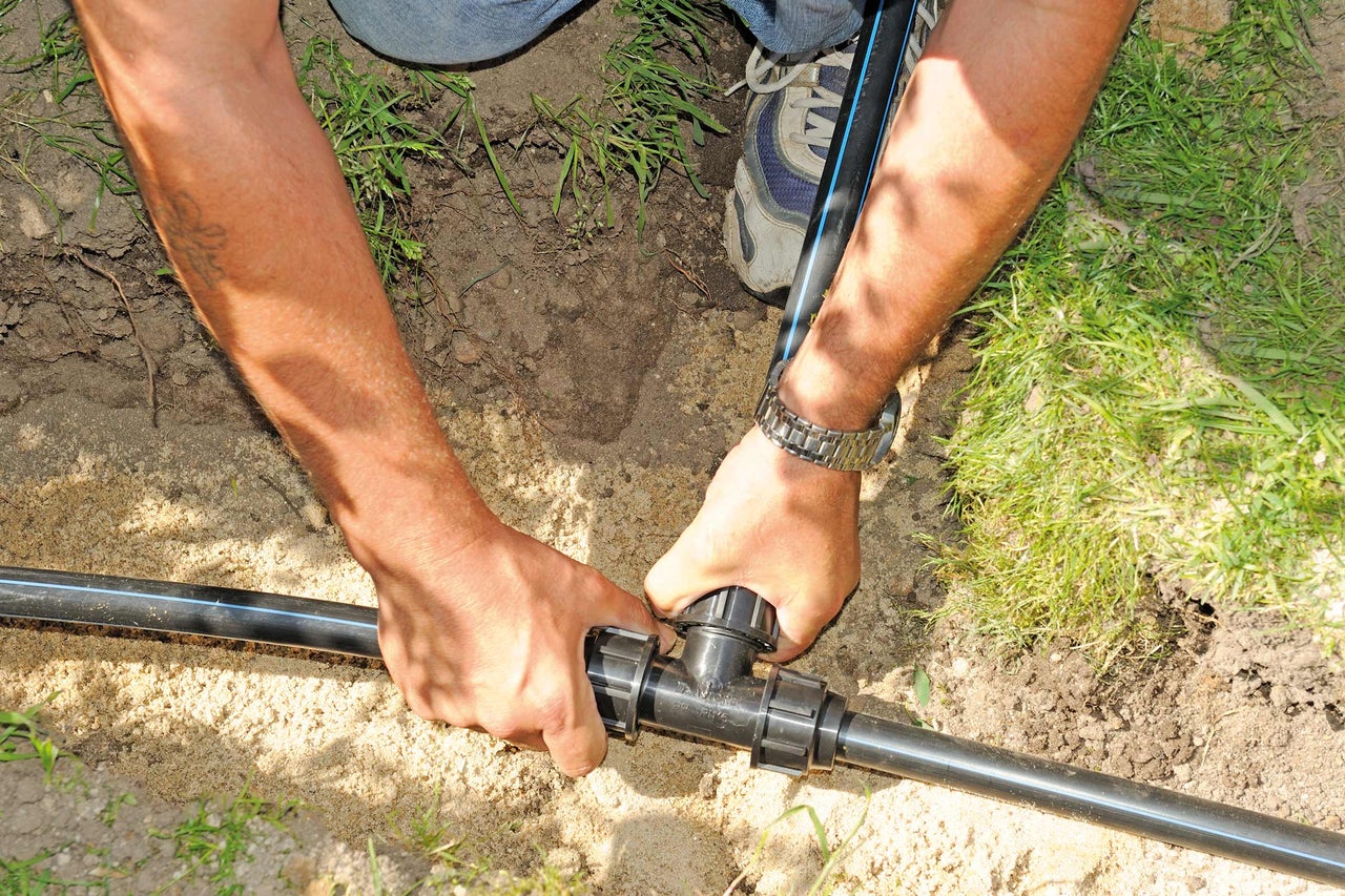 Une personne monte un raccord en T sur un tuyau d'irrigation noir dans le jardin.