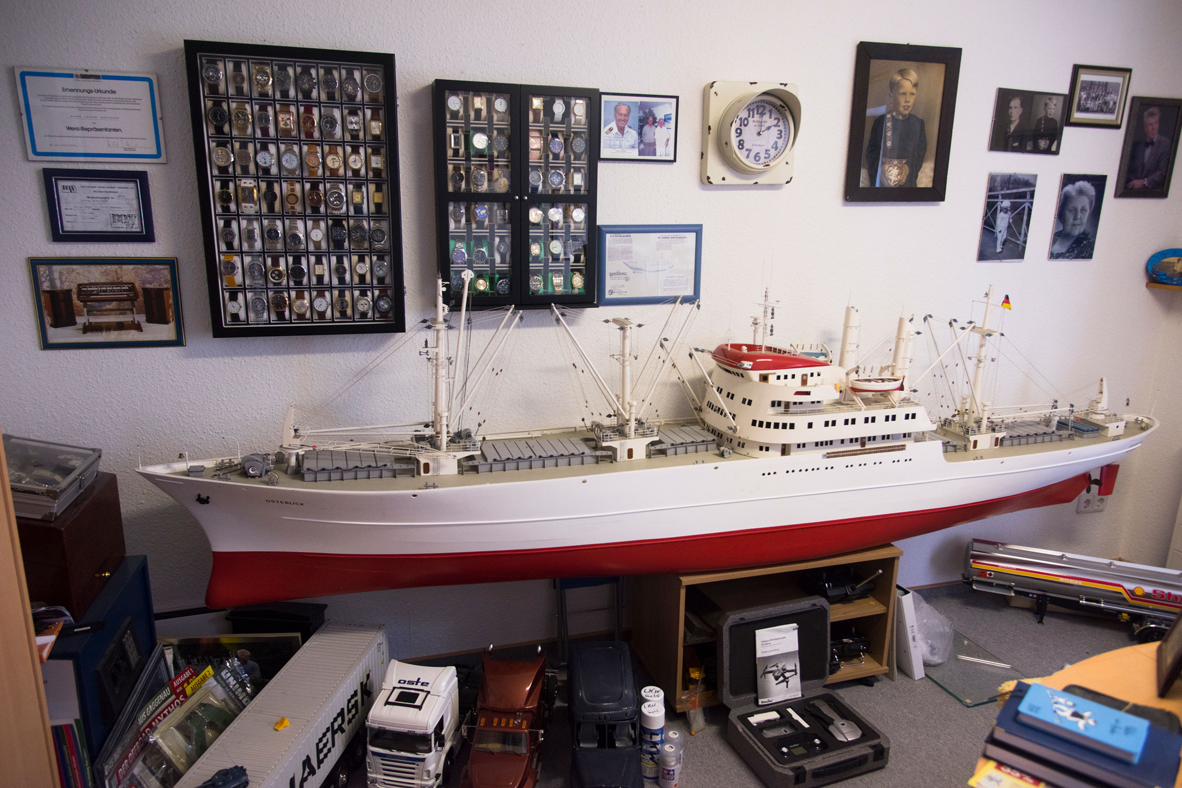 Modellschiff in einem Raum mit Uhrensammlungen und Fotos an der Wand.