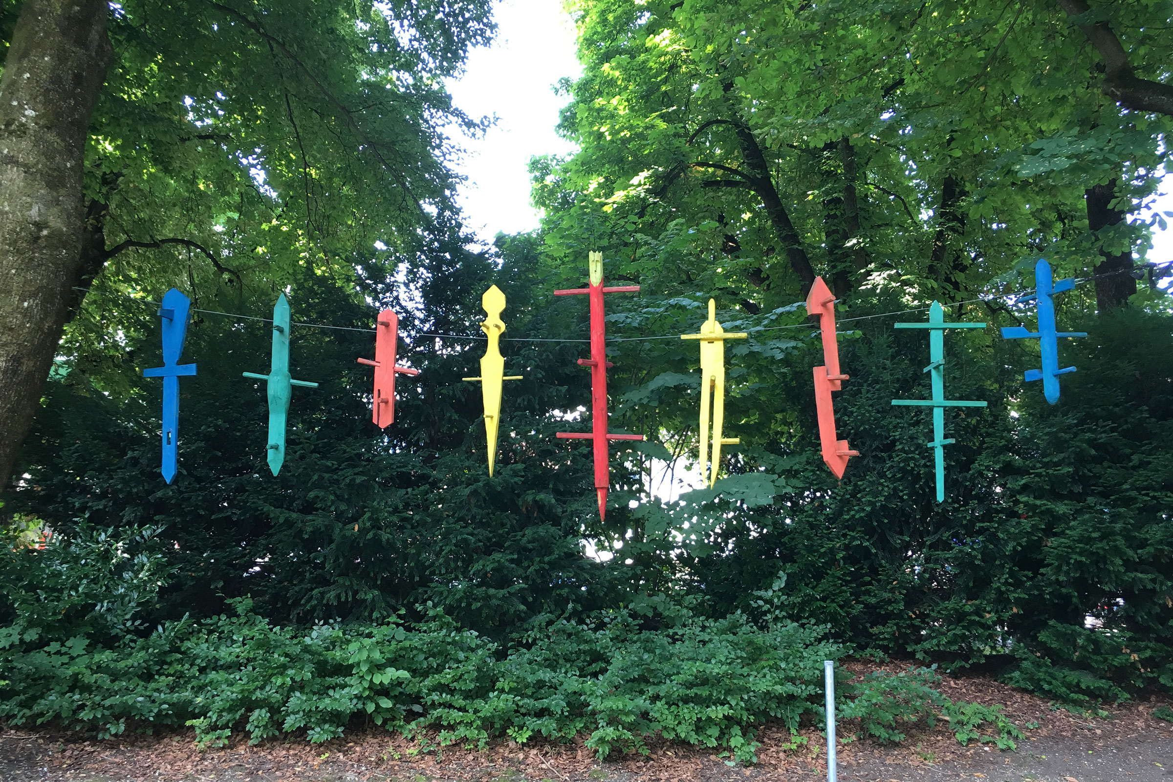 Dekorative Figuren hängen an einer Schnur im Freien, umgeben von Bäumen und Büschen.