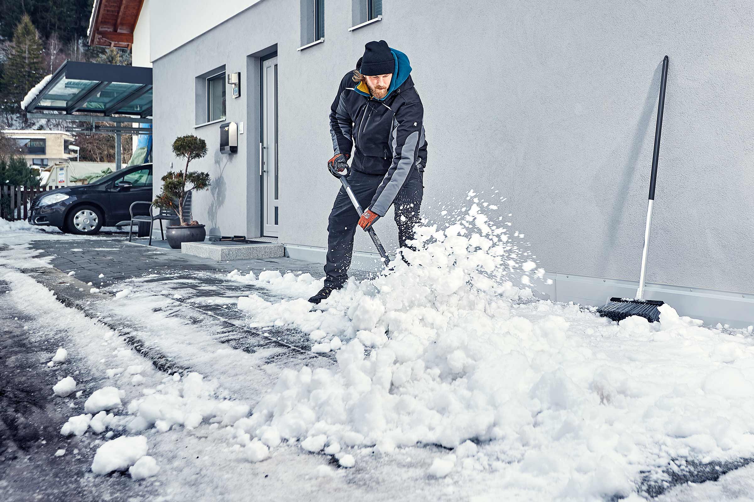 Mann schaufelt Schnee vor Haus mit Schneeschaufel