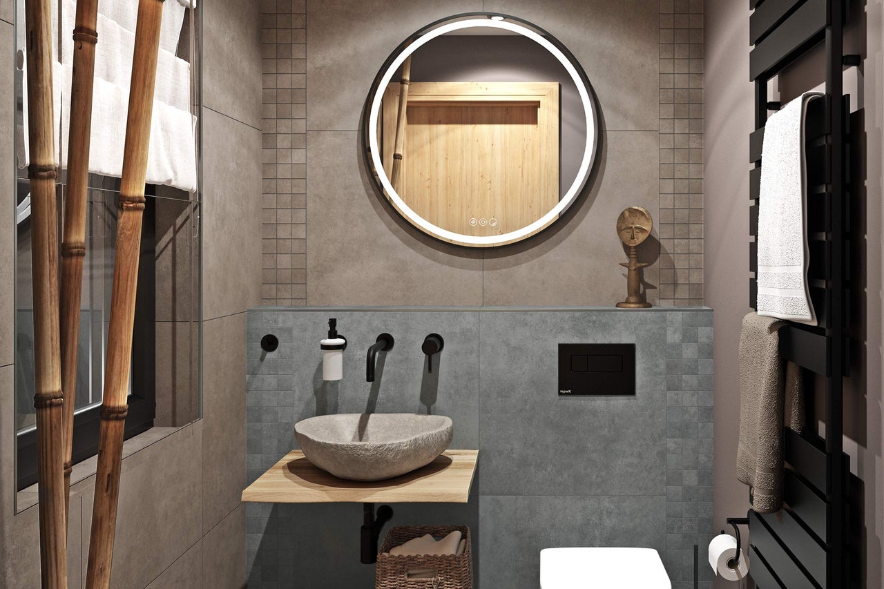 Salle de bains moderne avec miroir rond lumineux, vasque à poser en pierre naturelle sur console en bois, robinetterie noire et carrelage gris.