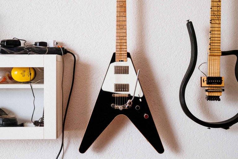 An der Wand hängen eine V-förmige E-Gitarre und eine weitere Gitarre mit einem Rahmen als Korpus.
