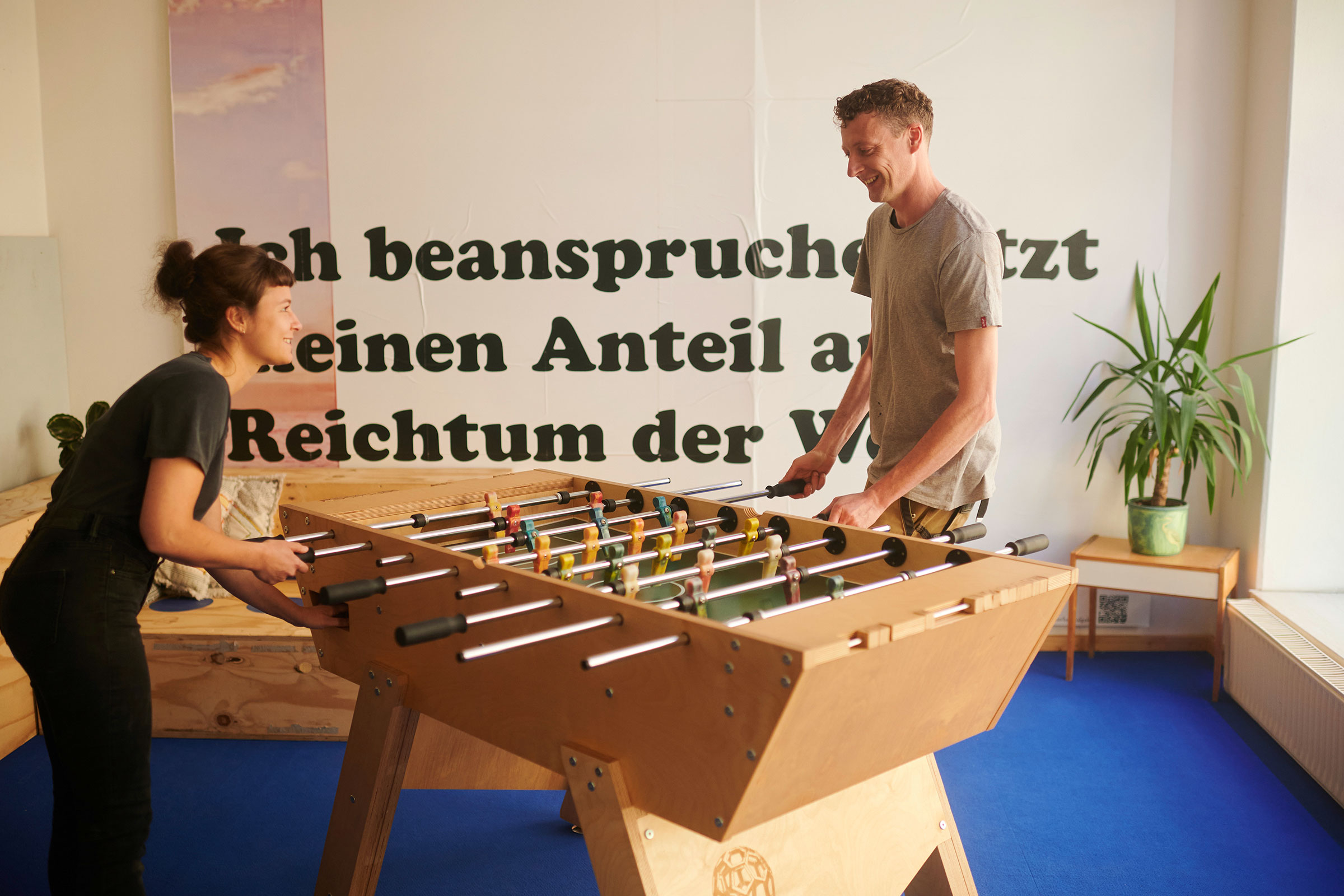 Zwei Personen spielen an einem Tischfußballtisch in einem hellen Raum.