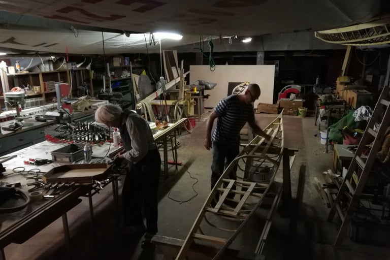 Werkstatt mit Personen, Holzboot und Werkzeugen