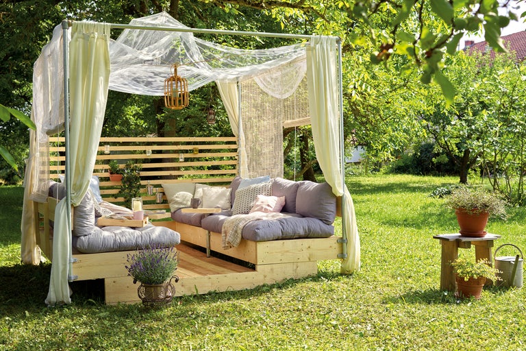 Scène de jardin avec terrasse en bois couverte, coussins d'assise et plantes