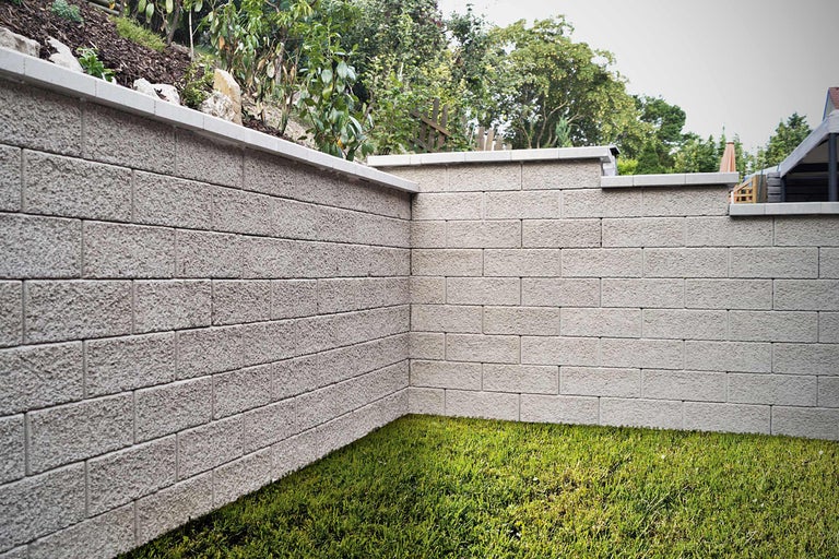 Un mur de jardin en blocs de béton avec une pelouse au premier plan.