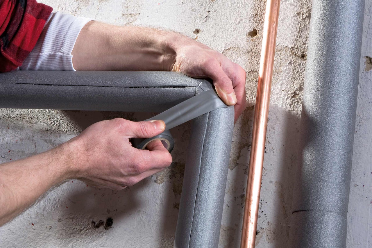Une personne fixe l'isolation des tuyaux avec du ruban isolant sur une canalisation.