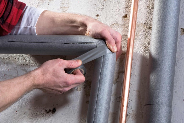 Une personne fixe l'isolation des tuyaux avec du ruban isolant sur une canalisation.