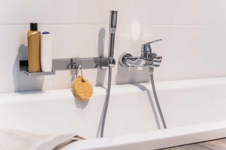 Badezimmerarmatur mit Handbrause, Duschgel und Badeschwamm an einer Badewanne