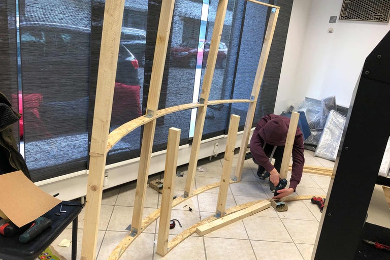 Ein Mann montiert eine Holzkonstruktion mit einem Akkuschrauber in einem Innenraum.