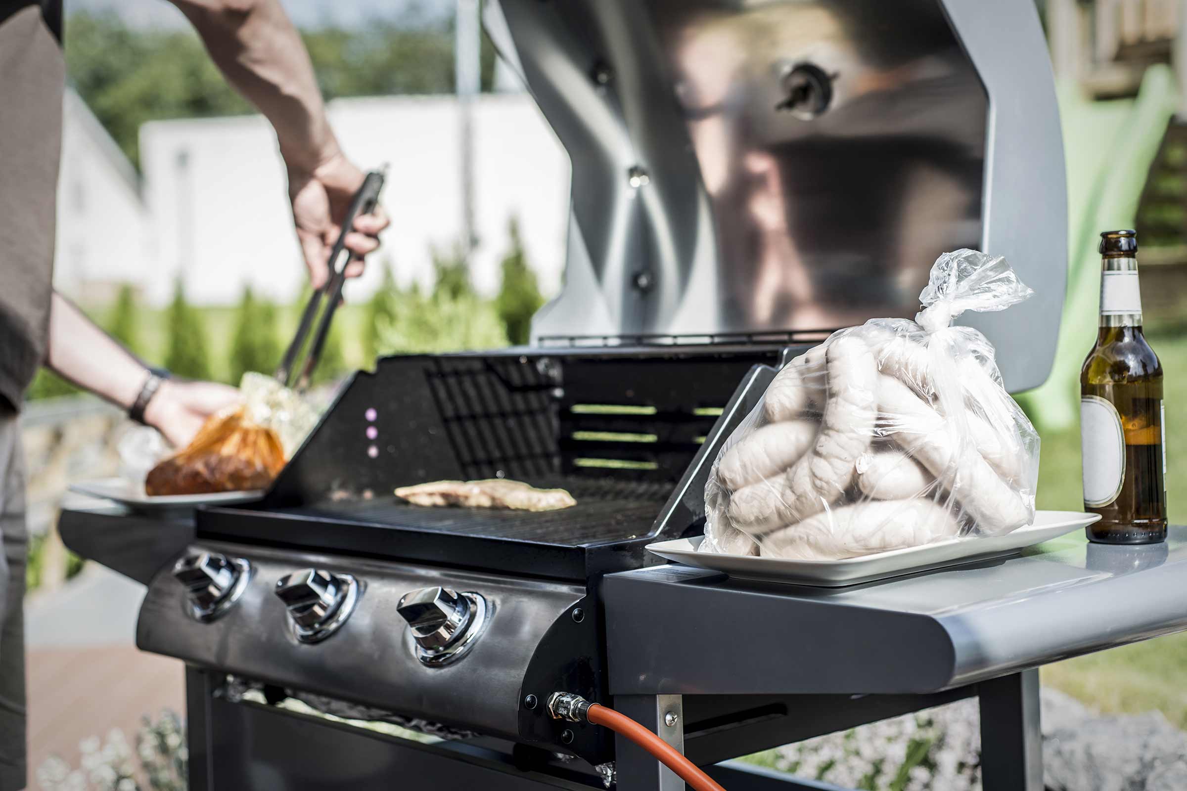 Scène de barbecue avec grill, saucisses et personne utilisant une pince de barbecue