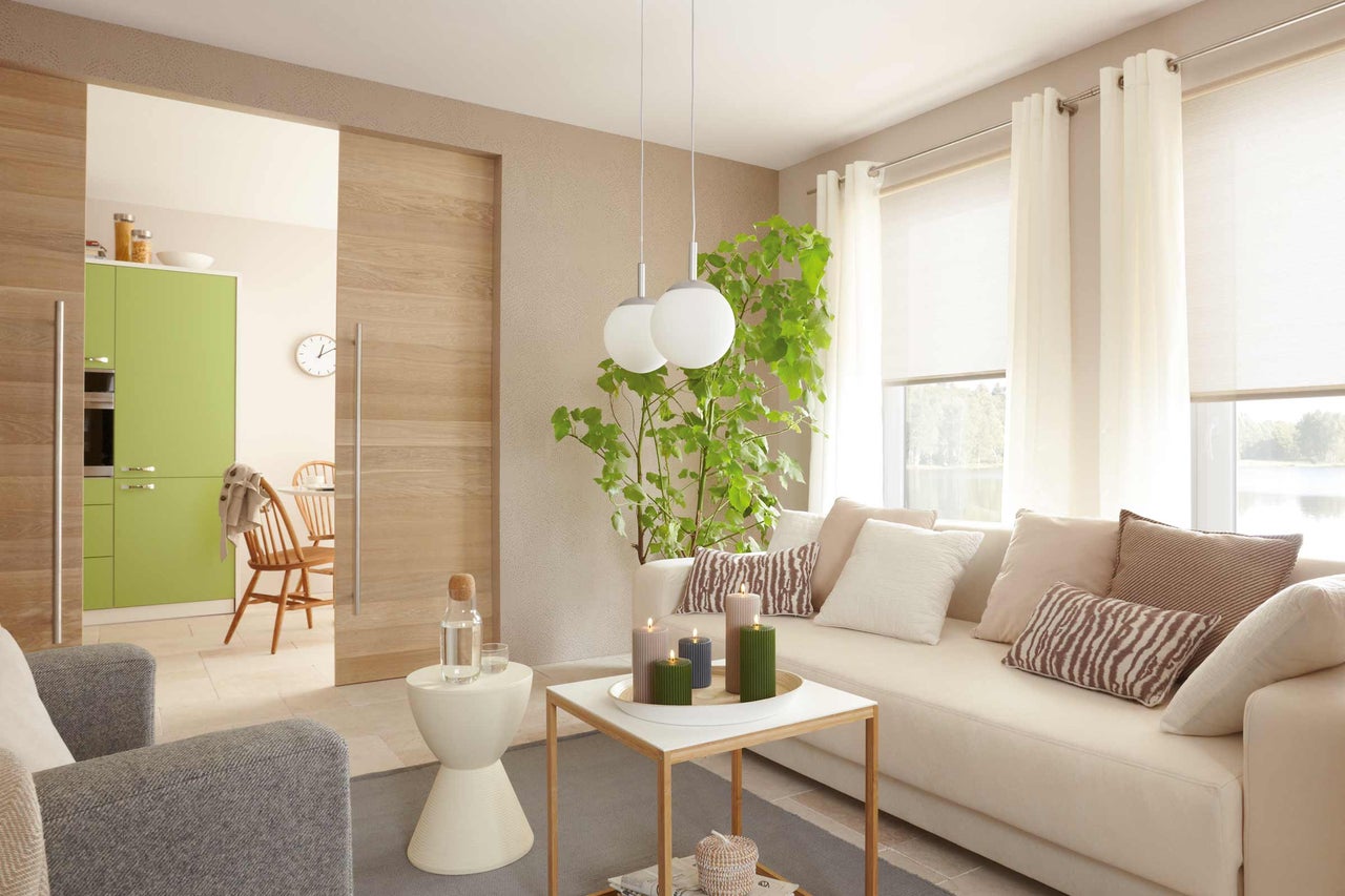 Espace de vie lumineux avec canapé, table, plante d'intérieur, rideaux et porte coulissante vers la salle à manger