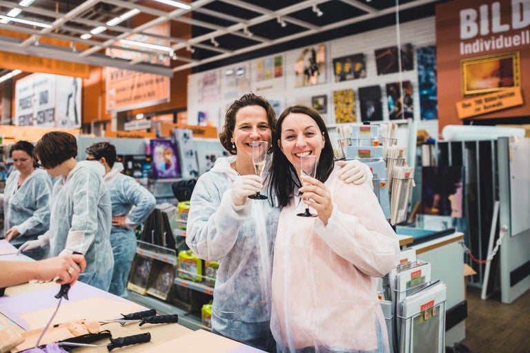 Deux clientes en combinaison de protection et gants trinquent au champagne dans le magasin Hornbach.