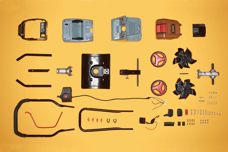 Einzelteile eines Rasenmähers auf gelbem Hintergrund