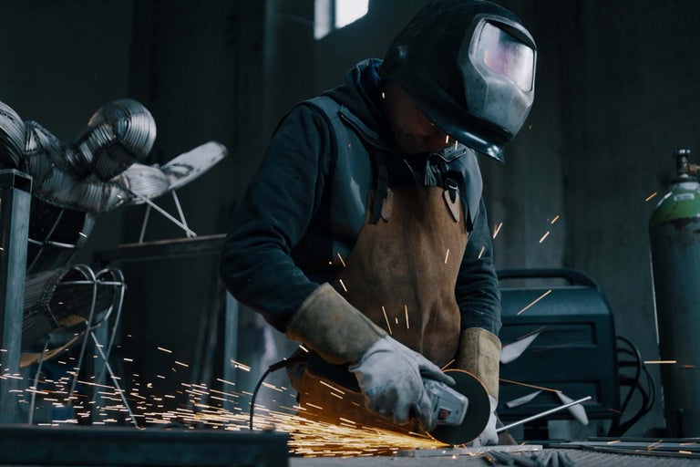 Homme avec casque de protection et tablier utilise une meuleuse d'angle dans un atelier