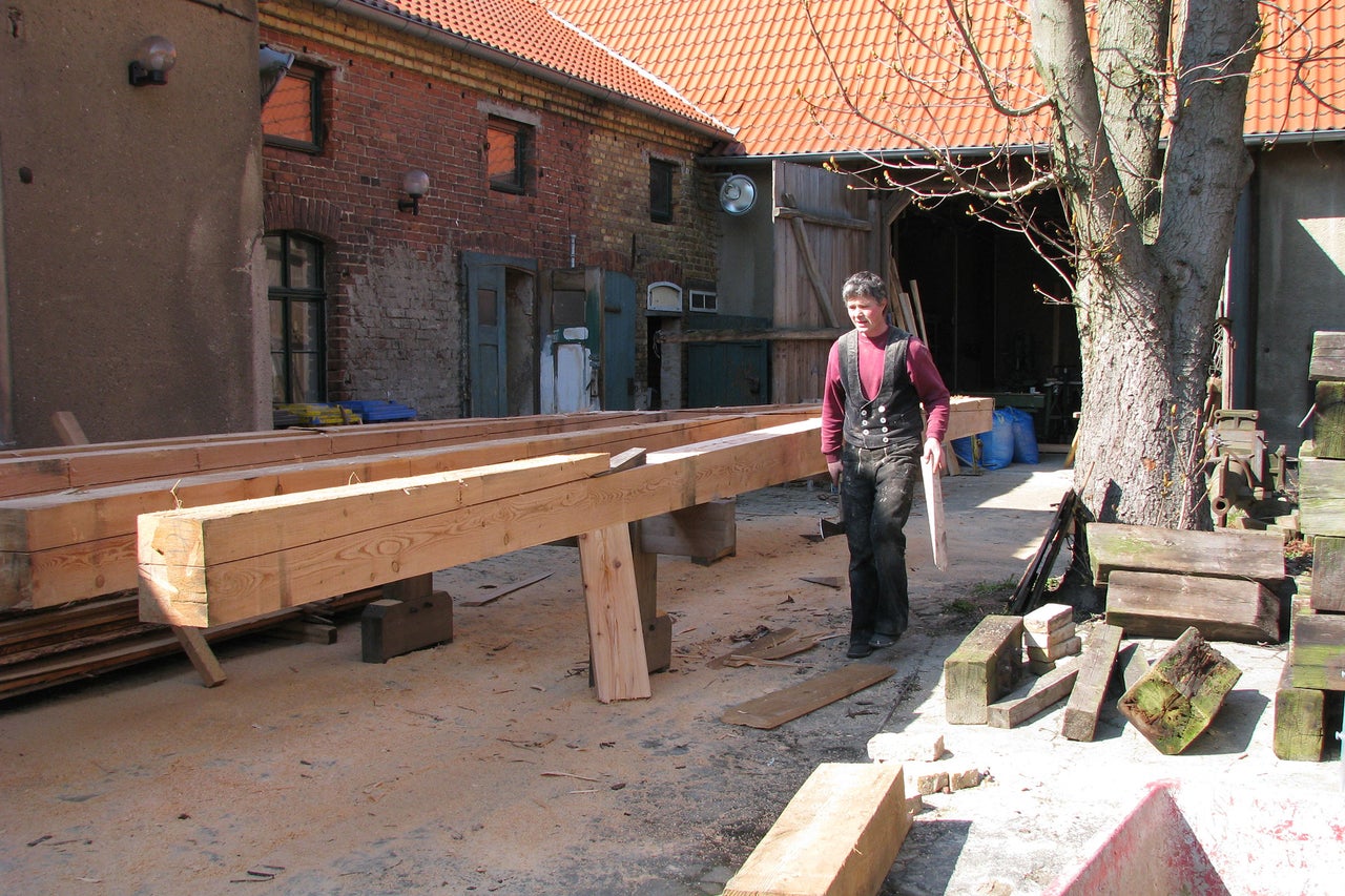 Homme en tenue de charpentier travaillant avec des poutres en bois à l'extérieur