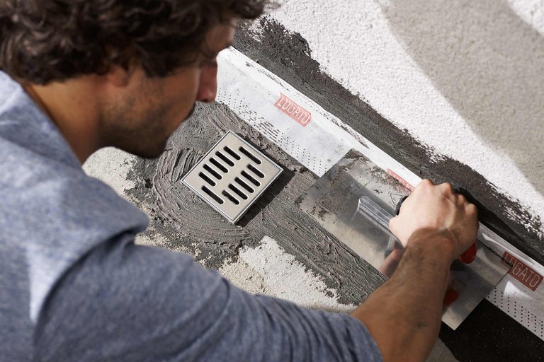 Artisan installant un drain de sol avec manchette d'étanchéité et spatule