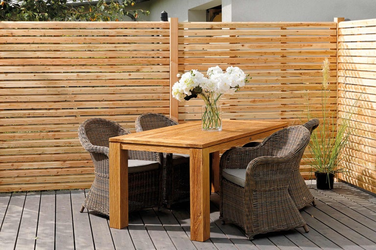 Scène avec table en bois, chaises en rotin et clôture en bois sur une terrasse.